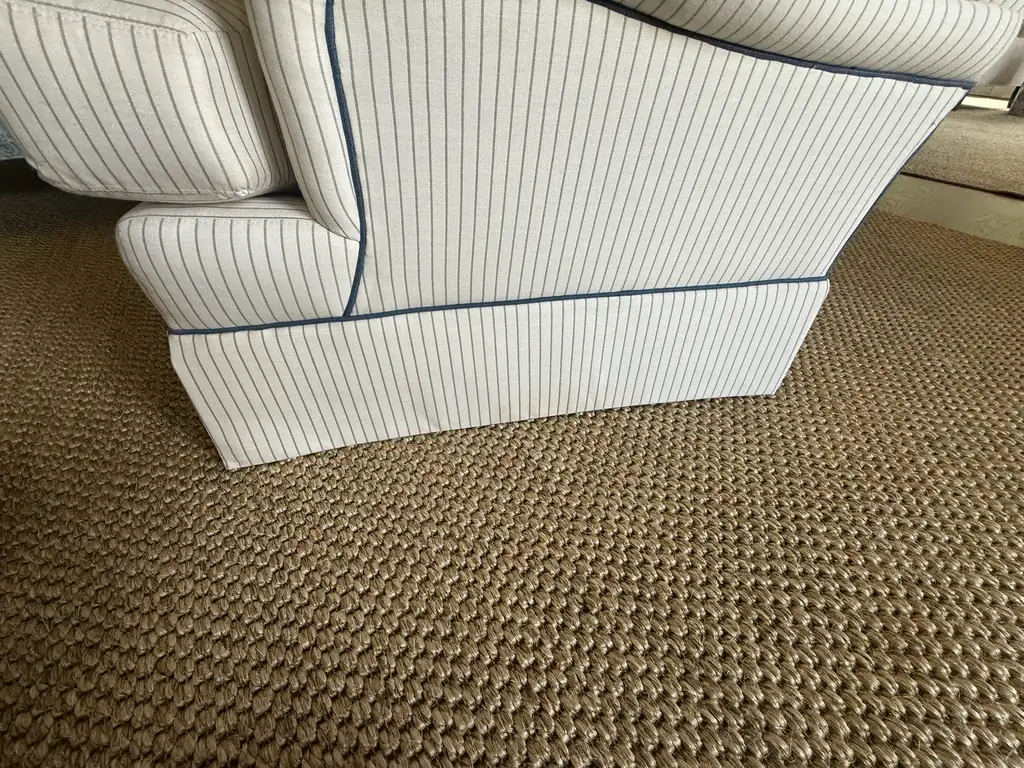 Close-up of a tight basket-weave jute rug beside the skirted base of a striped upholstered armchair