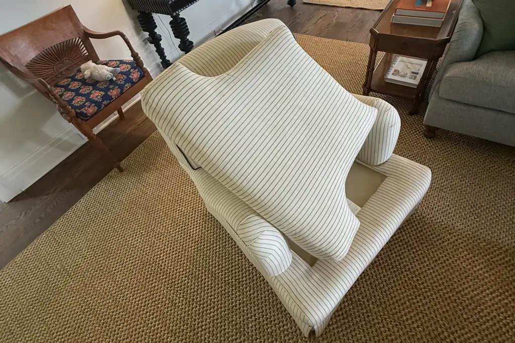 Striped upholstered armchair tipped back so the jute rug underneath can be reached during spot cleaning